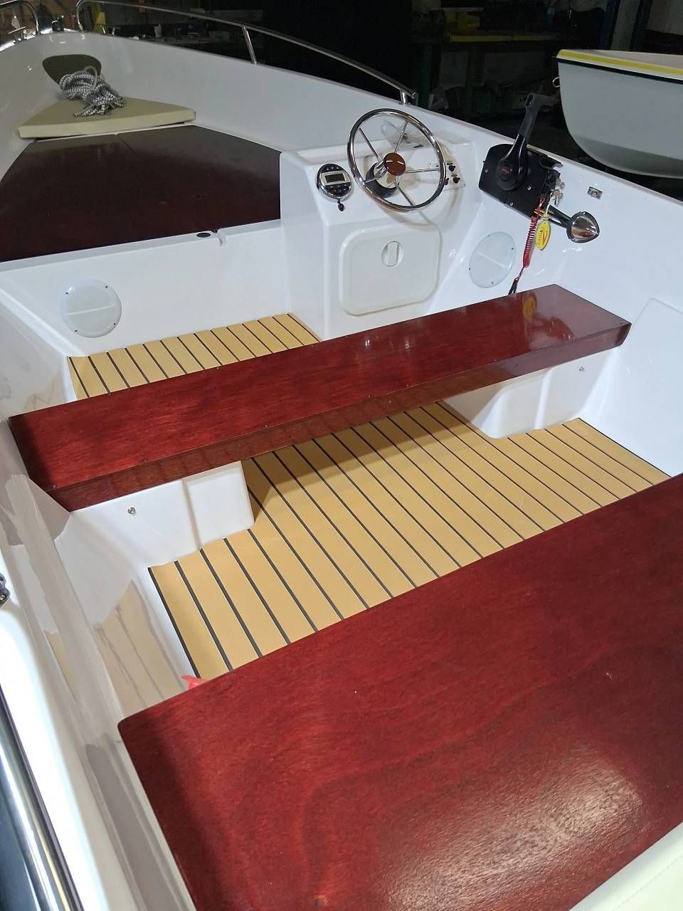 Abitacolo di una barca con panche in legno, ponte beige e volante.