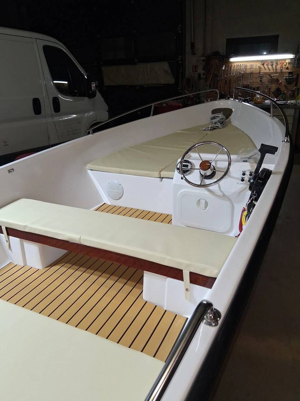 Interno di una piccola imbarcazione con sedili beige, ponte in legno e volante, ormeggiata di notte.