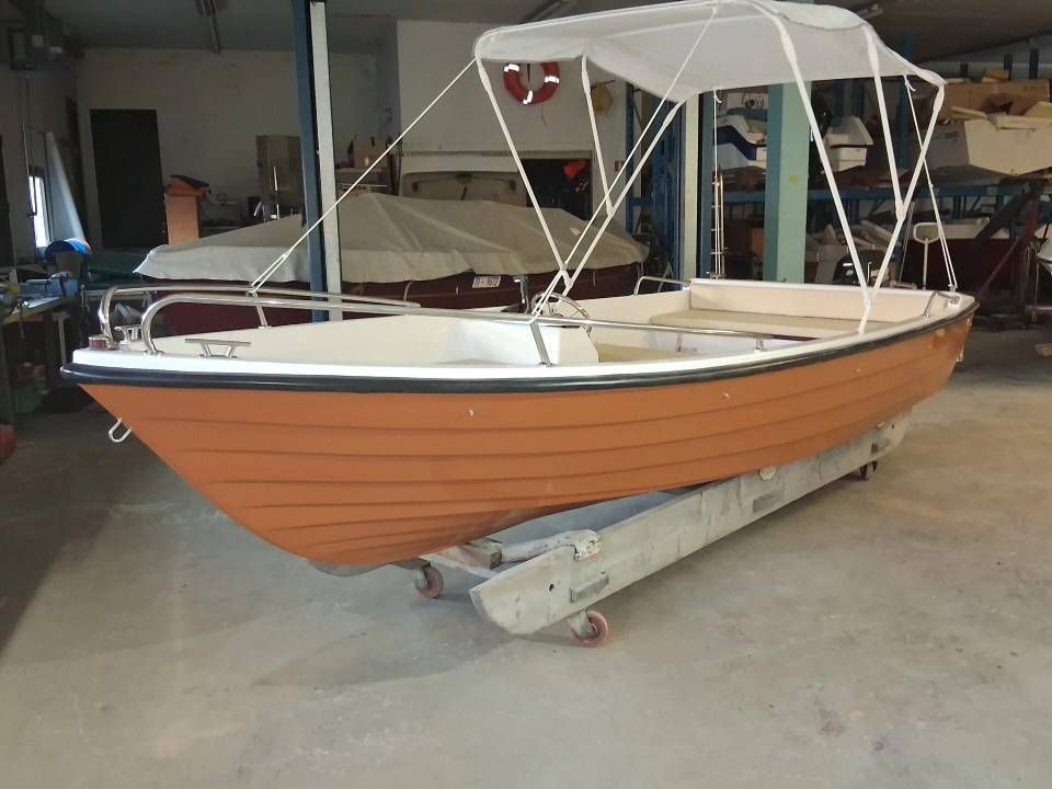 Piccola barca di legno arancione su un rimorchio in un garage, con tettuccio e finiture bianche.