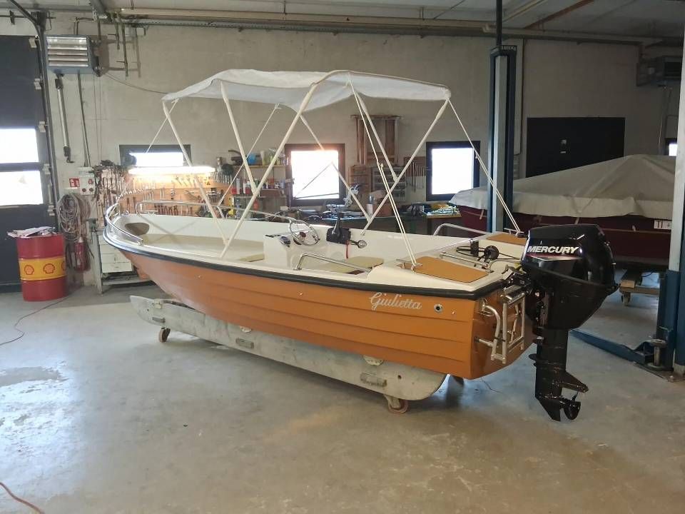 Motoscafo in legno con tettuccio bianco parcheggiato in un garage accanto a un'altra barca coperta.