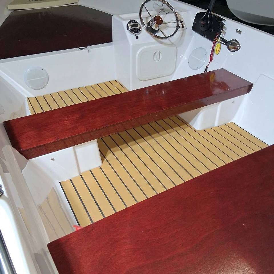 Interno della cabina di pilotaggio di una piccola barca a vela con panche in legno rosso e pavimento del ponte color beige.
