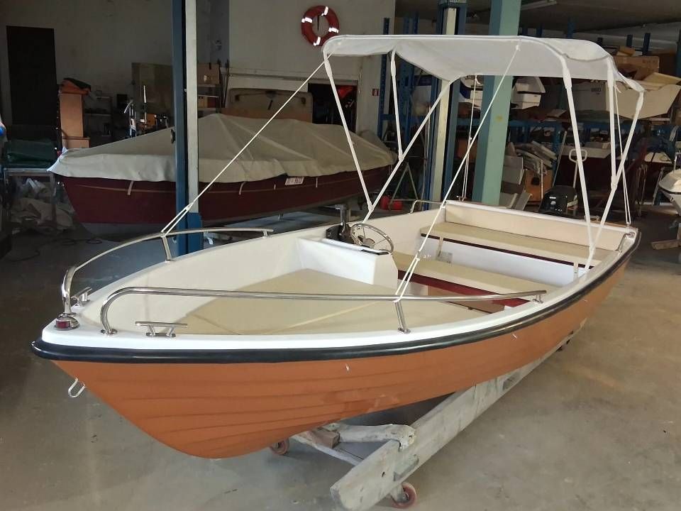 Piccola barca da pesca in legno con tettuccio bianco, parcheggiata su un rimorchio all'interno di un'officina.