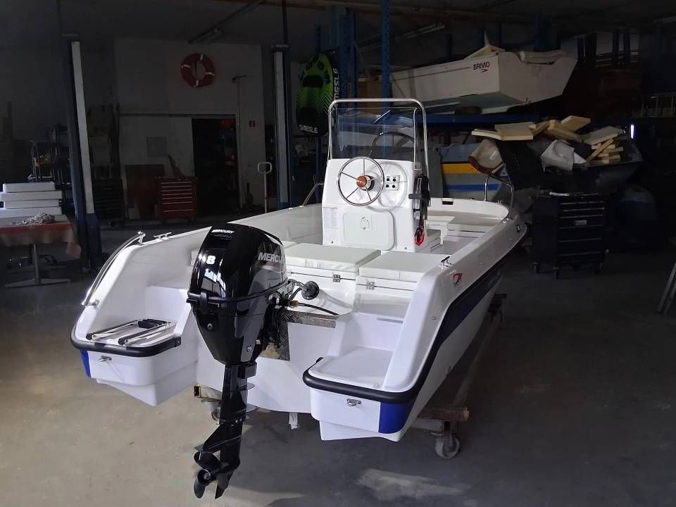 Motoscafo bianco su rimorchio in un'officina, con due motori fuoribordo visibili a poppa.