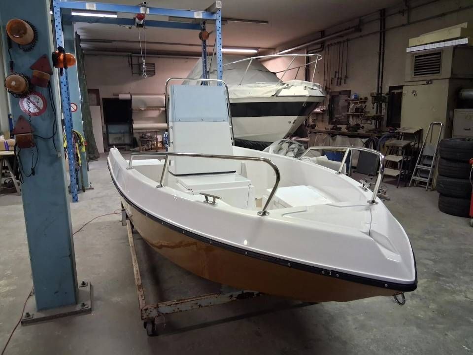 Motoscafo bianco su un sollevatore in un'officina al coperto, con una colonna di supporto blu nelle vicinanze.
