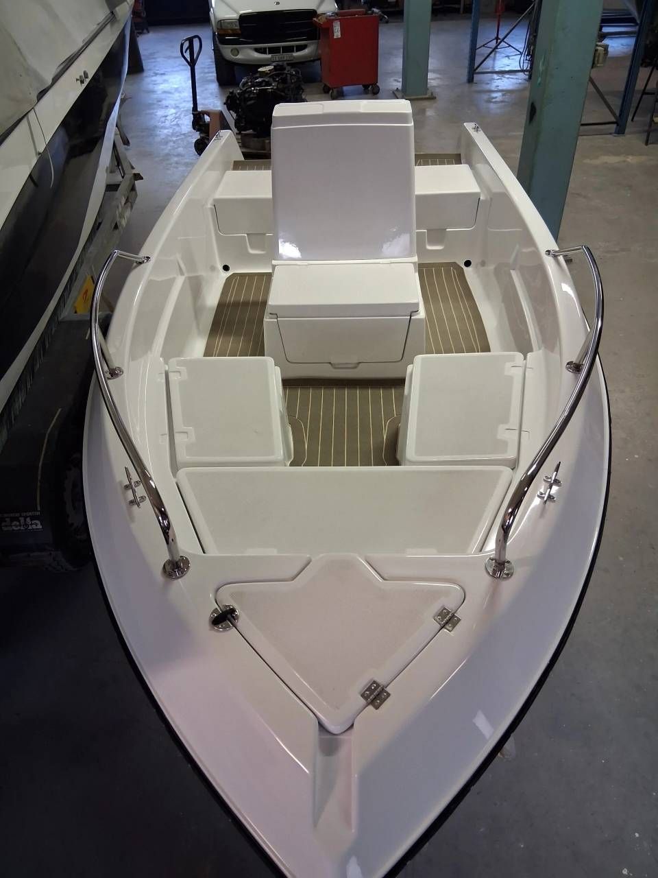 Motoscafo bianco visto di prua, con sedili beige vuoti in uno showroom al coperto.