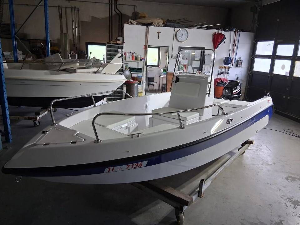 Piccola imbarcazione a motore bianca e blu all'interno di un'officina, appoggiata su un rimorchio.