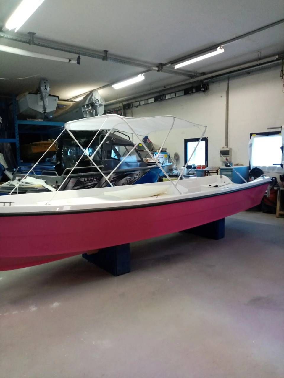 Barca rosa e bianca in un garage, con parabrezza e telo blu sopra.
