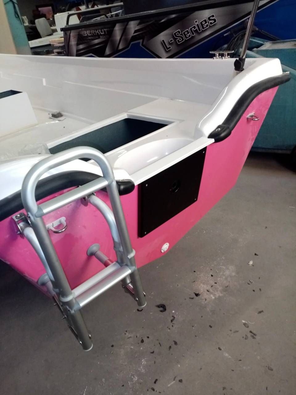Scafo di barca rosa e bianco con una scaletta di metallo in un'area di attracco o officina.