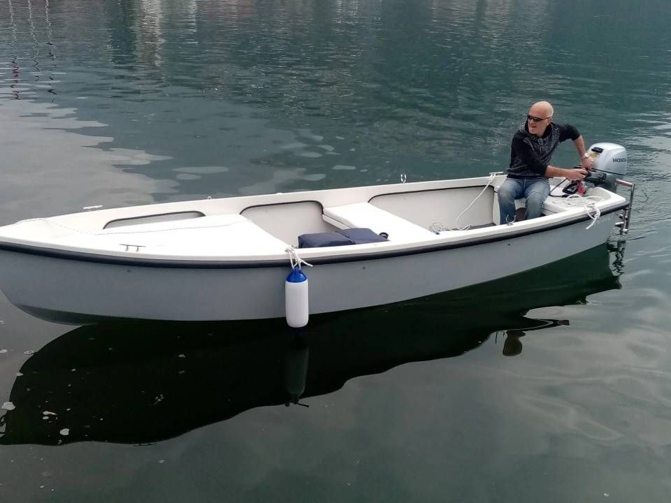Piccola barca bianca su acque calme con una persona seduta vicino alla poppa.