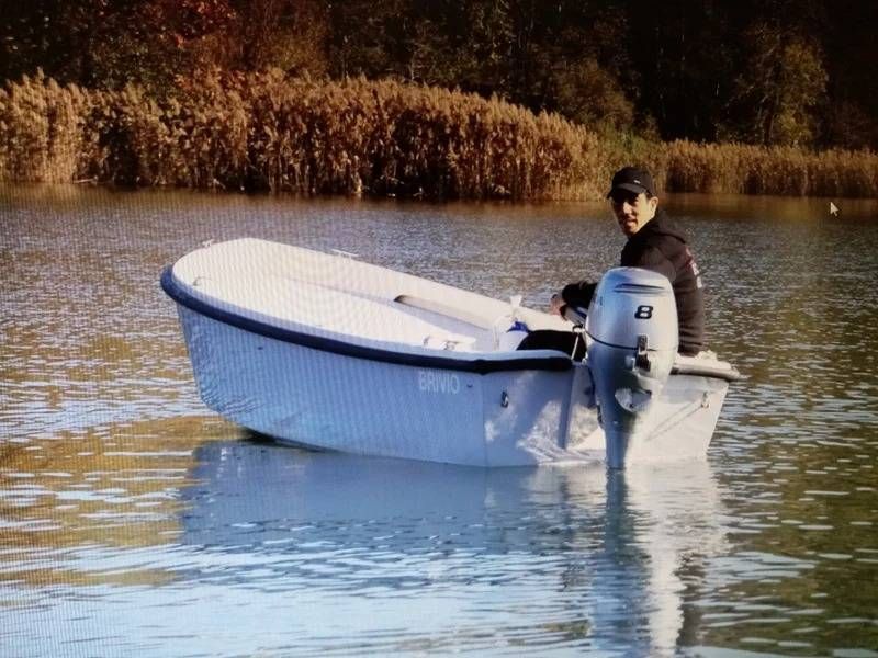Persona su una piccola imbarcazione con motore fuoribordo in acque calme, vicino a canneti sullo sfondo.