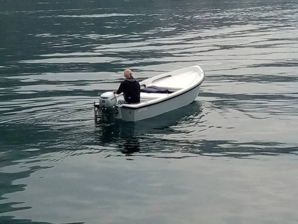 Persona a bordo di una piccola imbarcazione a motore bianca su acque calme, vista da dietro.