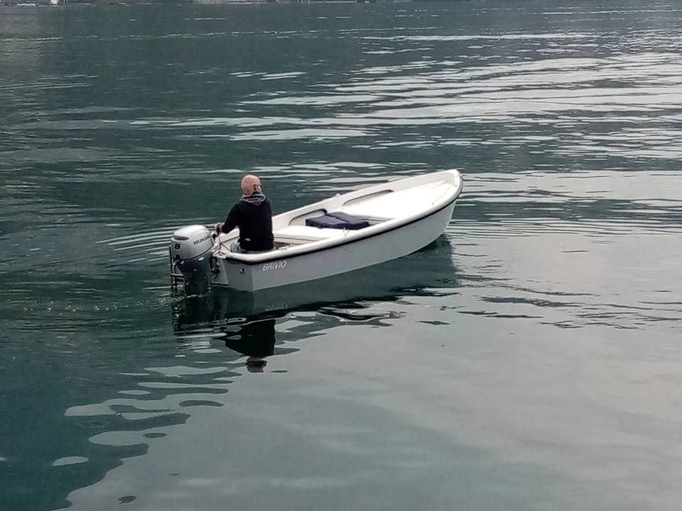 Piccola imbarcazione a motore bianca con una persona a bordo, su acque calme, vista dall'alto.