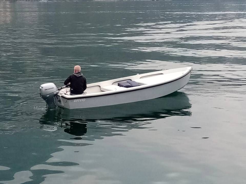 Piccola barca a motore bianca che galleggia su acque calme con una persona seduta vicino alla poppa