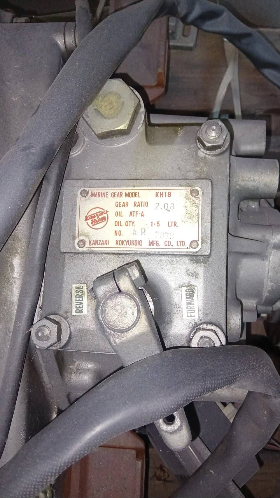 Primo piano di una pompa meccanica grigia o di un componente del motore con tubi flessibili e una targhetta metallica.