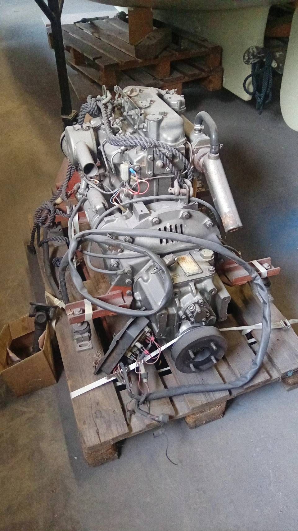 Un pallet pieno di componenti di motori, tubi metallici e cavi elettrici in uno spazio simile a un garage.