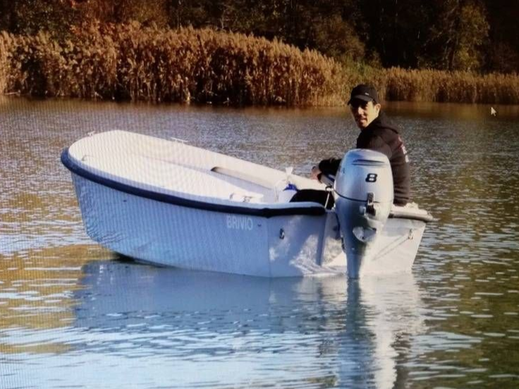 Persona su una piccola imbarcazione con motore fuoribordo in acque calme, vicino a canneti sullo sfondo.