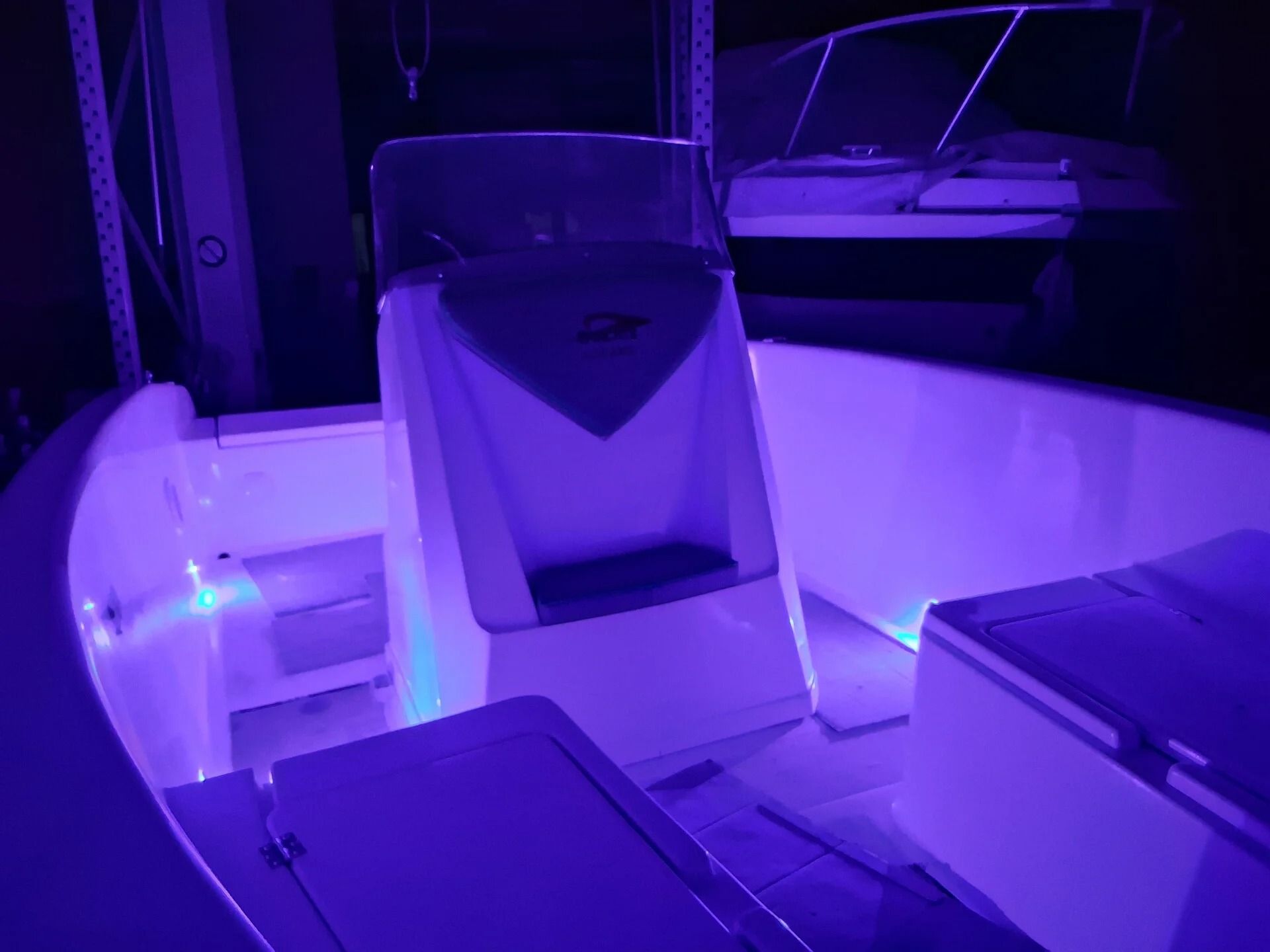 Abitacolo di una barca illuminato di viola con sedili vuoti e parabrezza di notte
