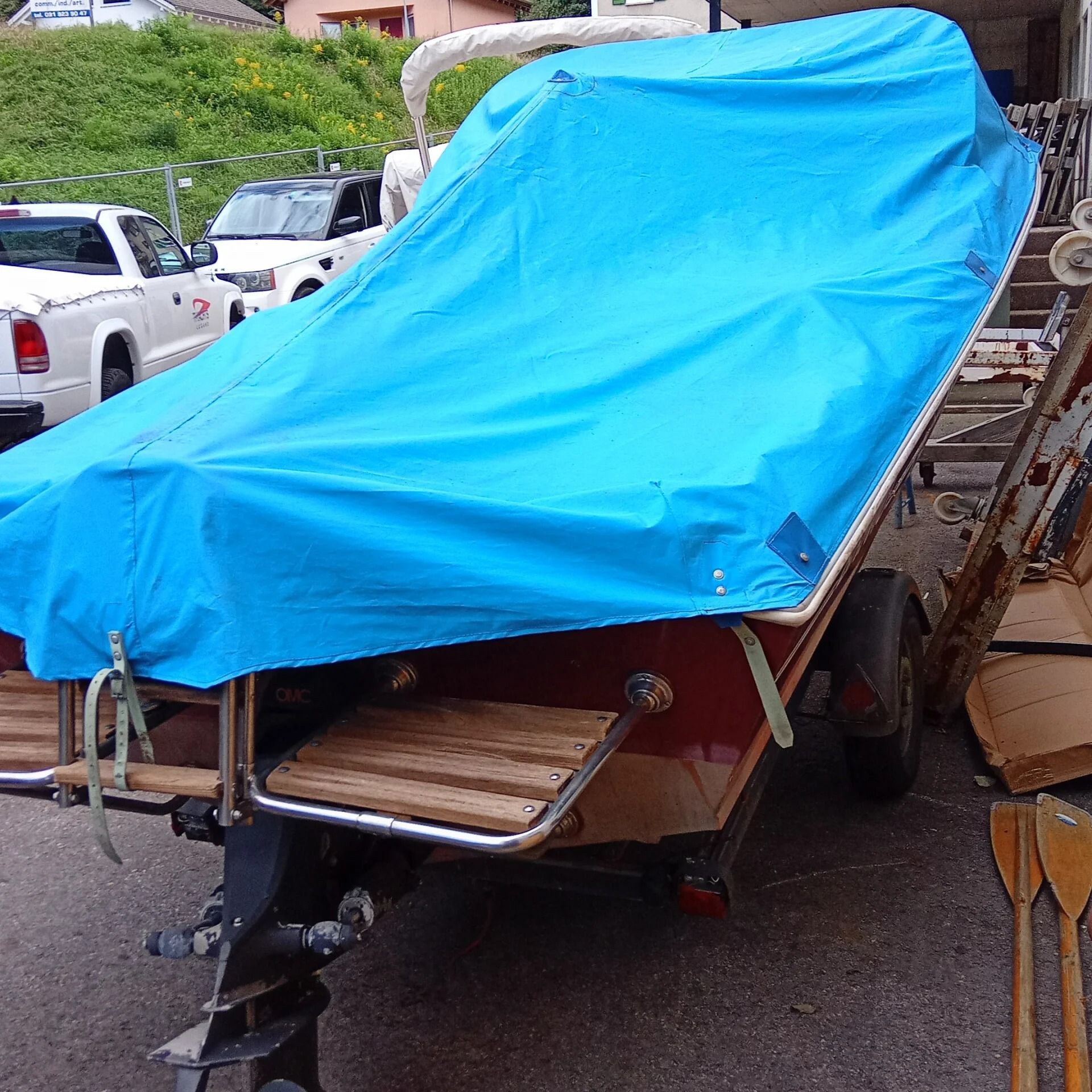 Ti Yachts Sagl
Piccola imbarcazione su un rimorchio coperta da un telo blu brillante, parcheggiata all'aperto in un piazzale.