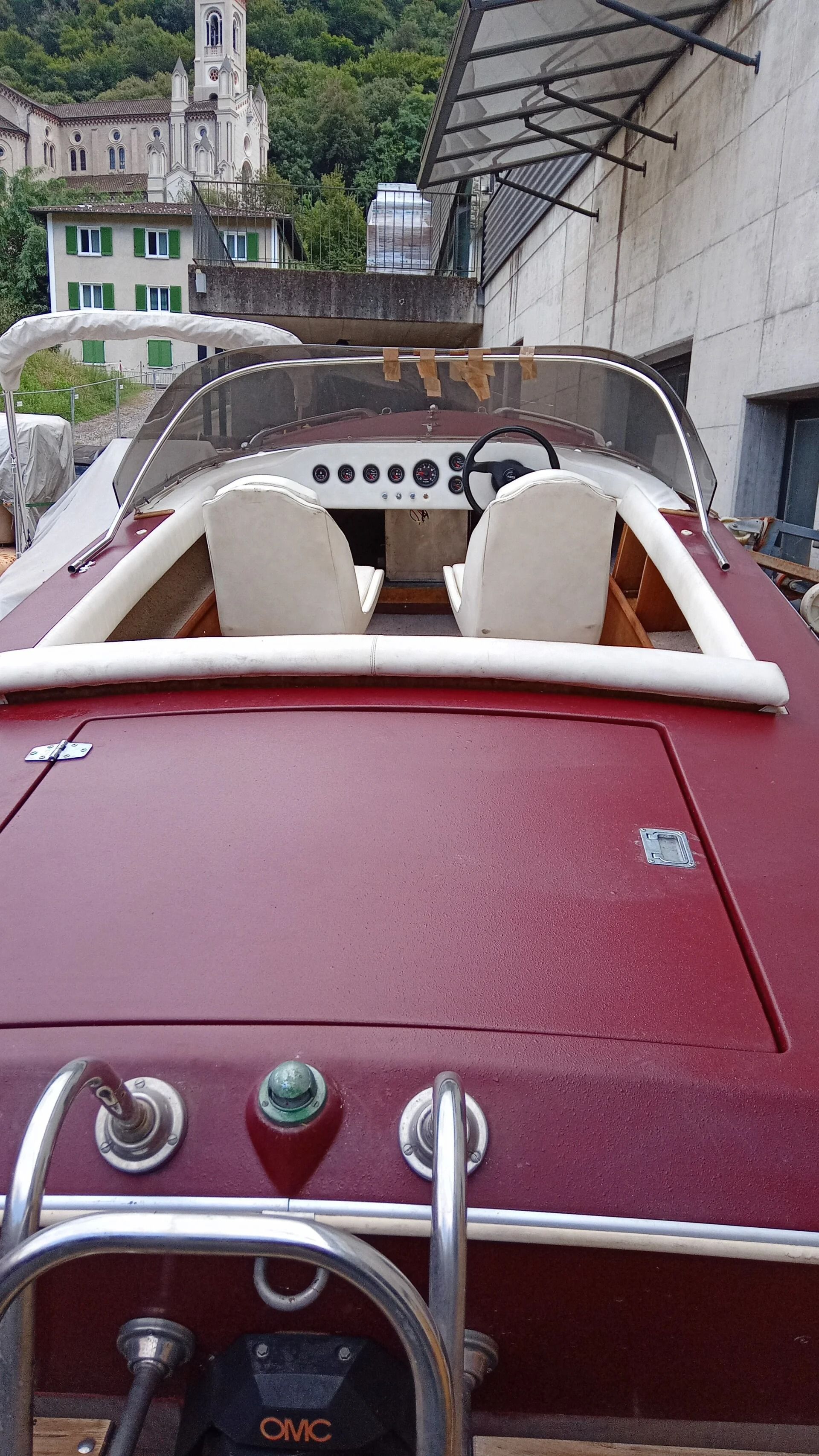 Motoscafo color bordeaux con sedili bianchi ormeggiato vicino a un muro di pietra e a una passerella coperta.