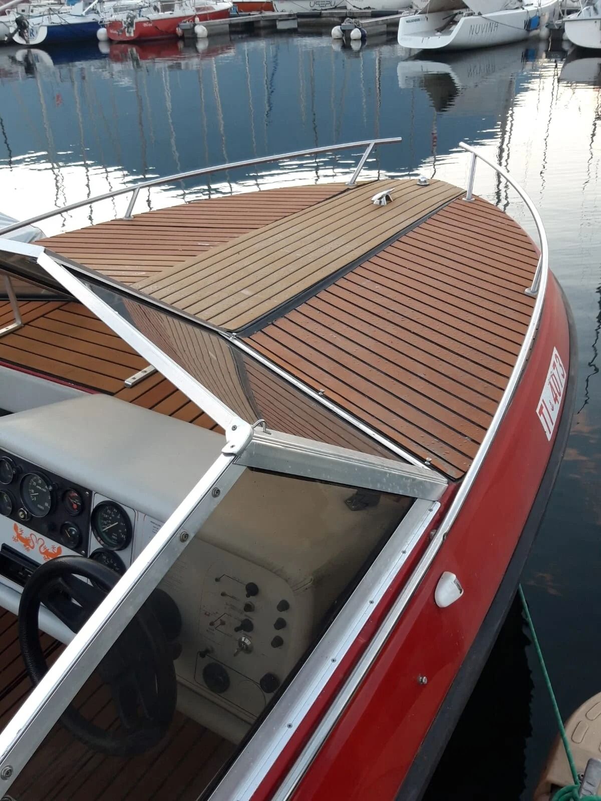 Ti Yachts Sagl
Barca rossa con telo di copertura color beige ormeggiata in un porticciolo turistico in acque tranquille.