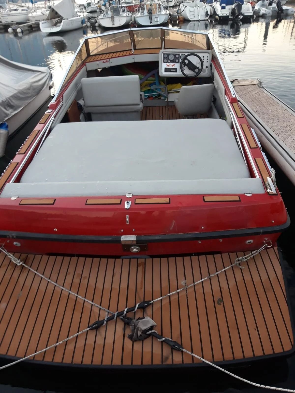 Ti Yachts Sagl
Barca di legno con tetto rosso e cuscini bianchi ormeggiata in un porticciolo, vista da poppa.