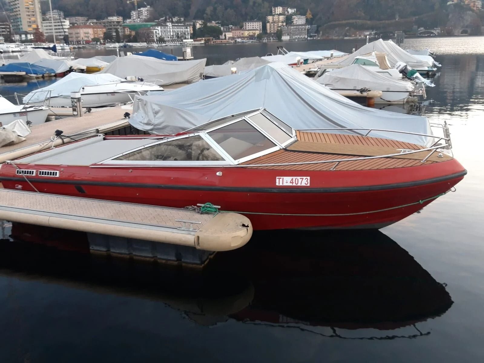 Ti Yachts Sagl
Barca rossa ormeggiata in porto accanto a yacht coperti e acque calme