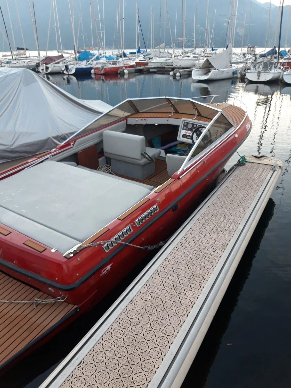 Ti Yachts Sagl
Motoscafo di legno rosso ormeggiato in un porto turistico accanto a barche a vela e moli.