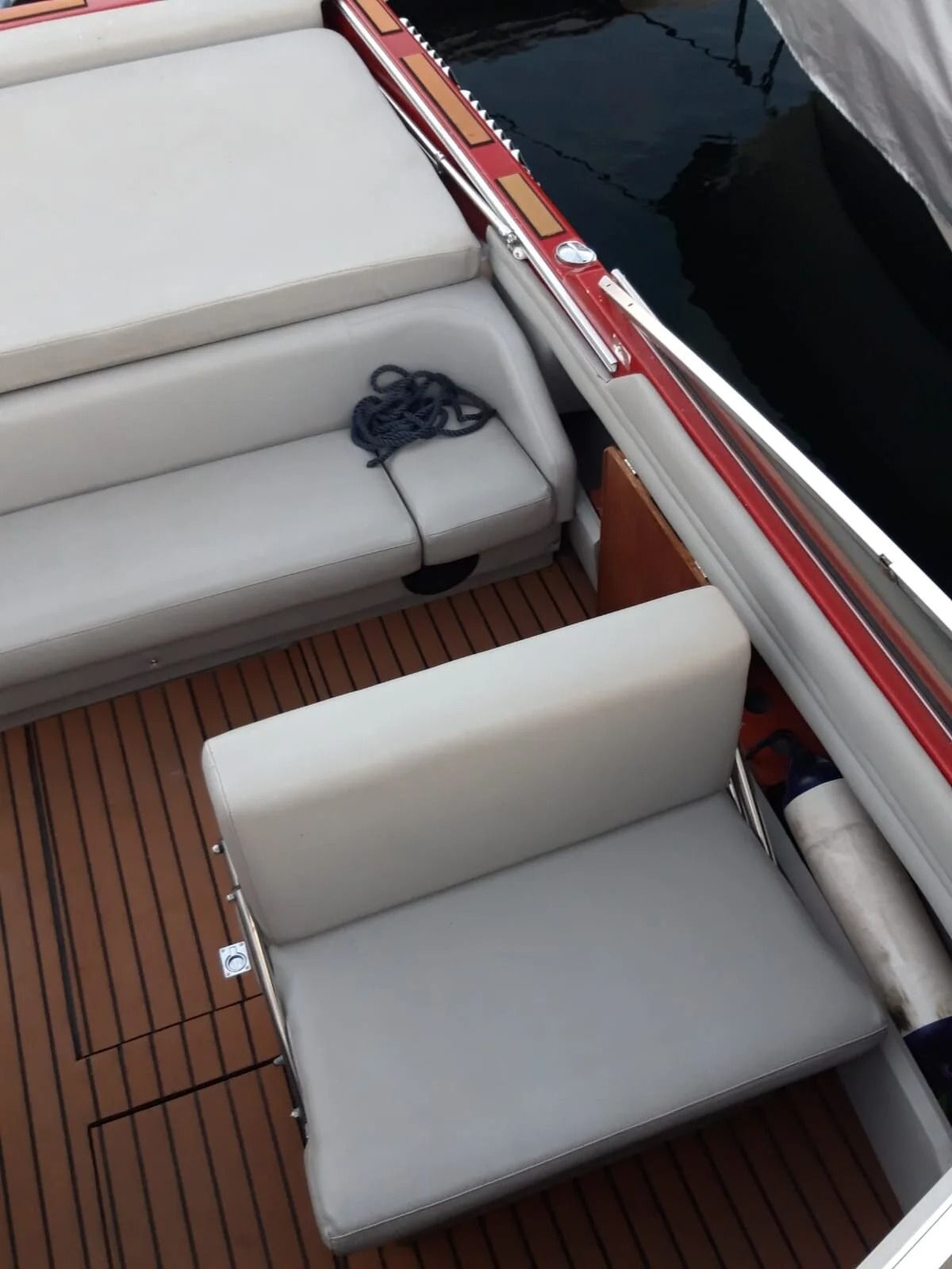 Ti Yachts Sagl
Ponte di una barca con sedili imbottiti bianchi, sedie grigie e pavimento a listelli di legno accanto ad acque scure.