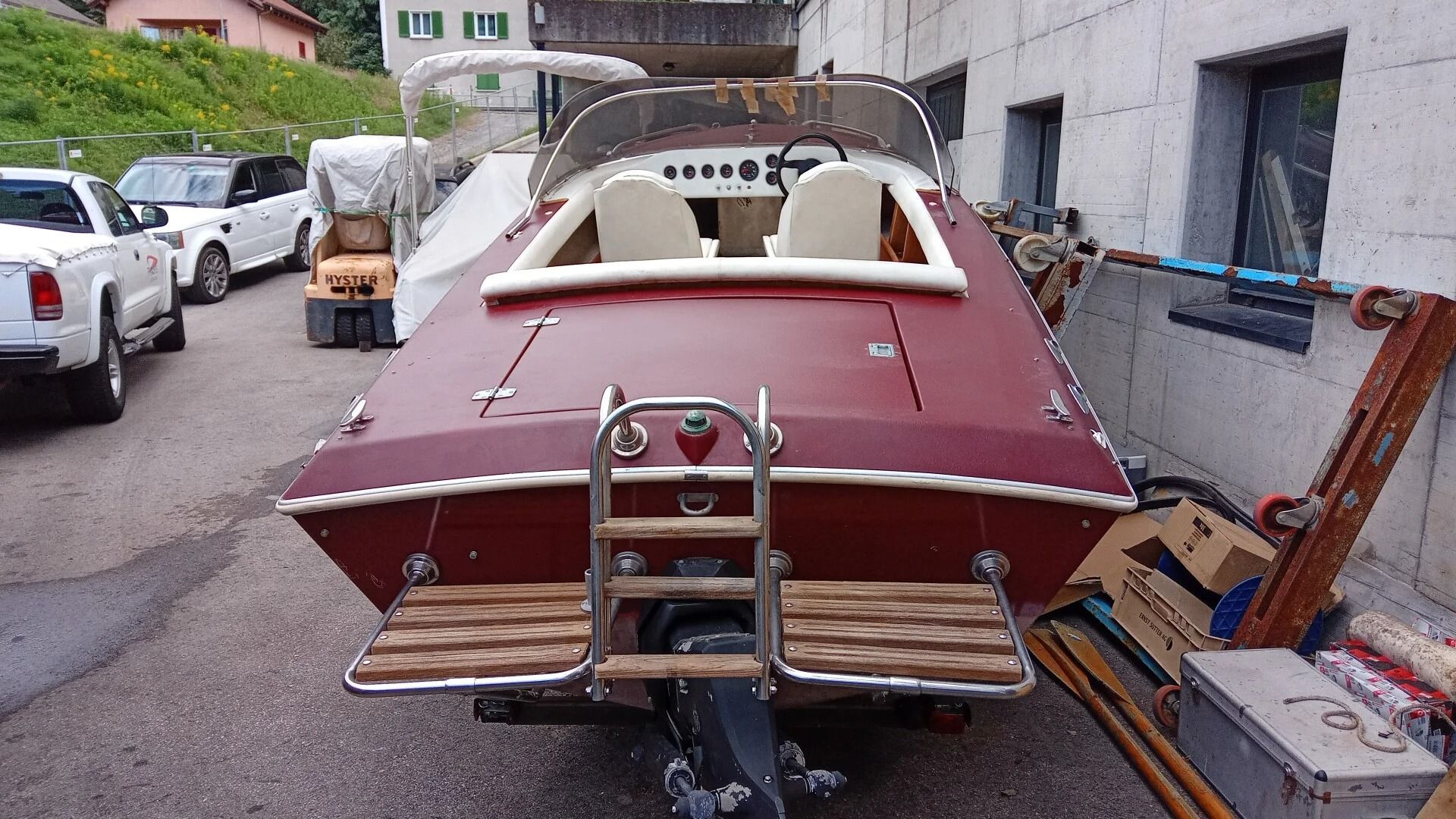Ti Yachts Sagl
Barca bordeaux e bianca parcheggiata in uno stretto vicolo accanto a edifici e automobili, con una scaletta a poppa