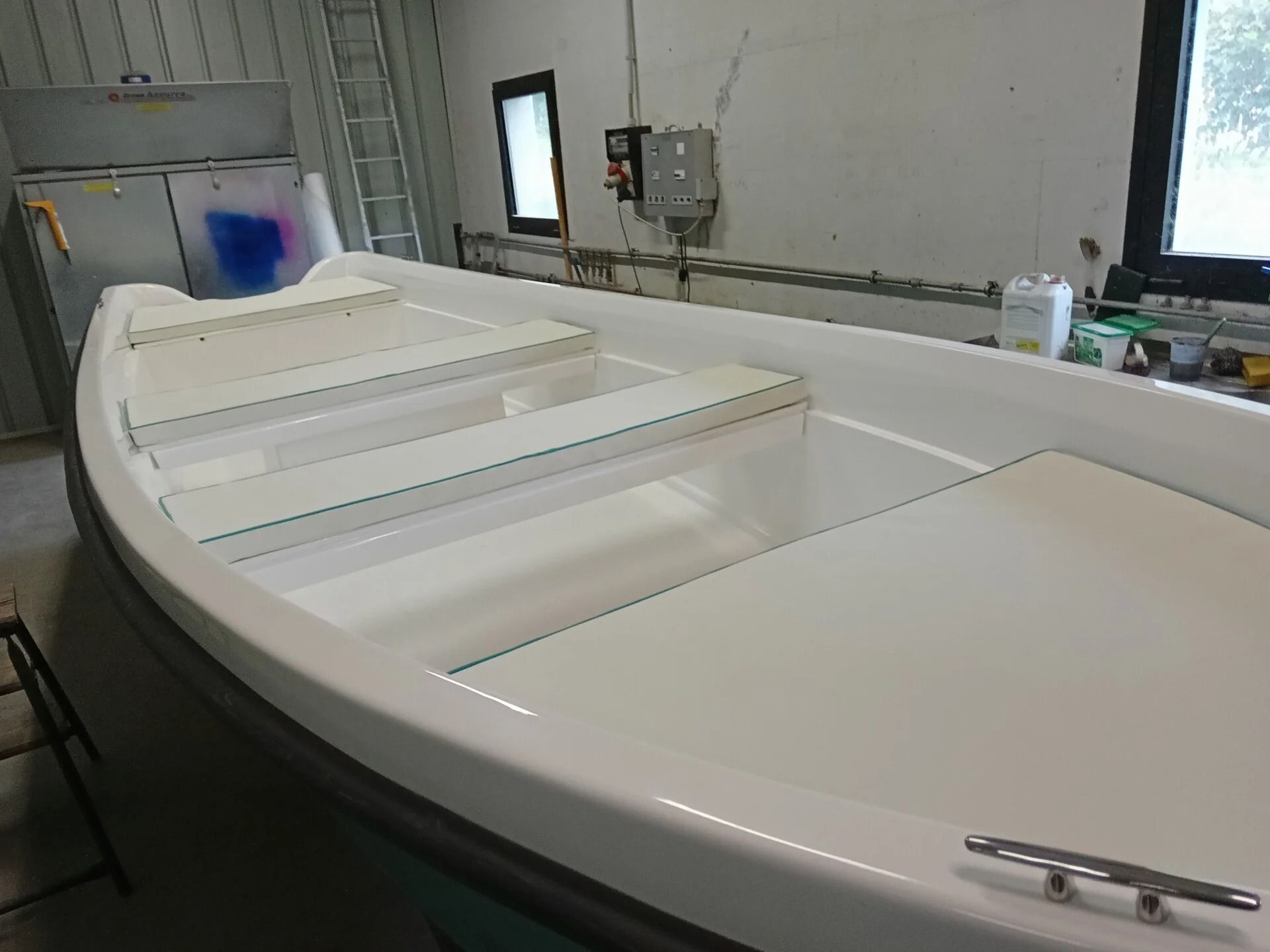 Ti Yachts Sagl 
Scafo di barca bianco in un'officina, visto da poppa con banchi interni e finestre sullo sfondo.