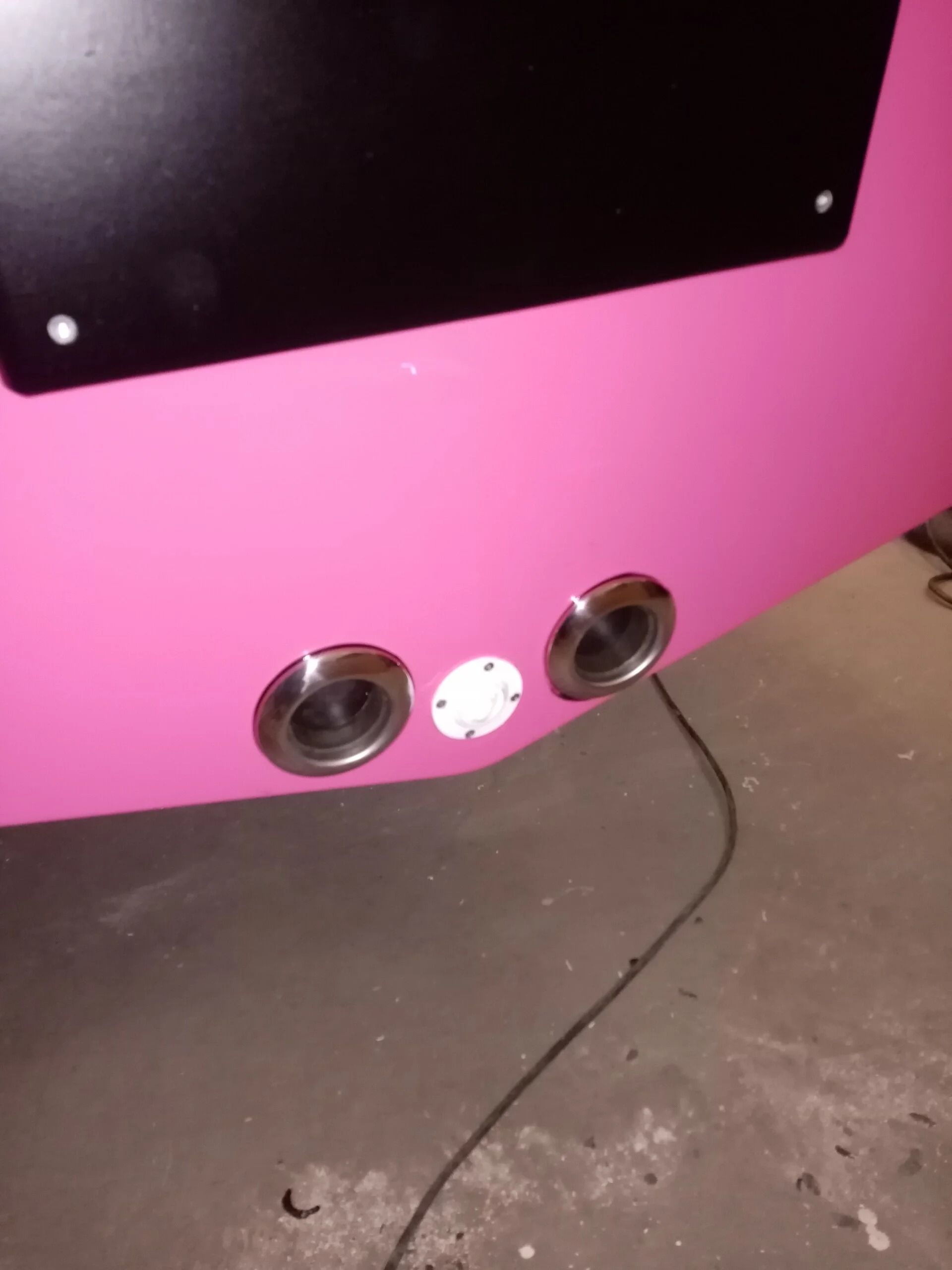 Base rosa per cabinato arcade con due porte rotonde e connettore bianco su pavimento in cemento.