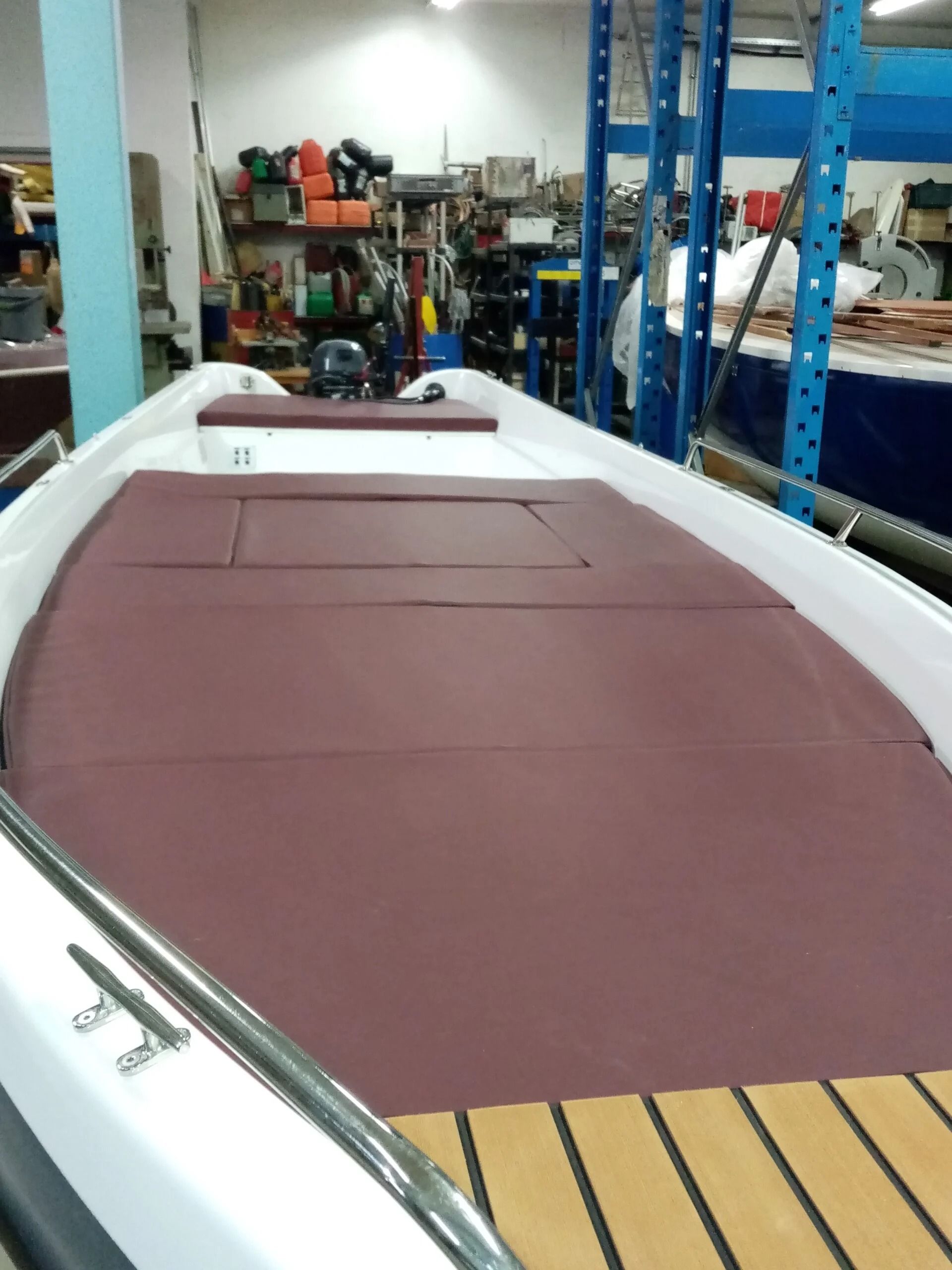 Grande scafo di barca ricoperto di color bordeaux in un'officina, con fiancate bianche e telai di supporto blu nelle vicinanze.