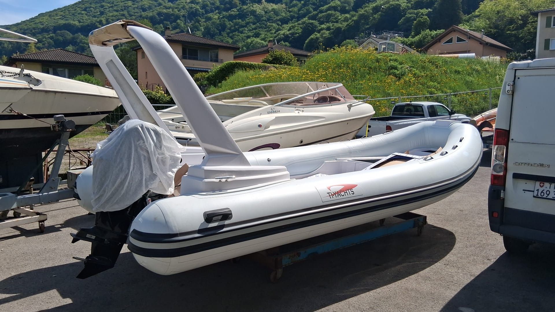 Ti Yachts Sagl 
Gommone bianco e grigio su un rimorchio in un parcheggio con le montagne sullo sfondo.