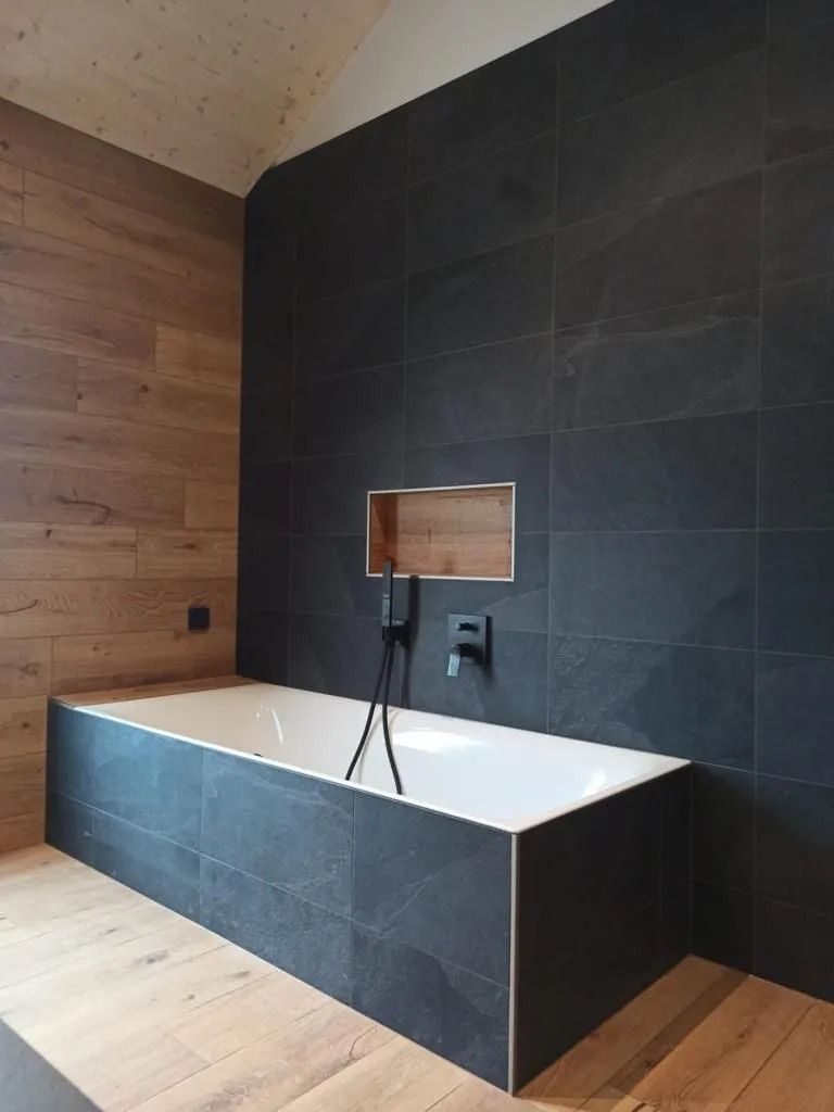 Une baignoire dans une salle de bain avec carrelage noir et parquet.