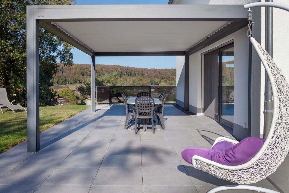 Un patio avec une table et des chaises sous pergola et un fauteuil suspendu.