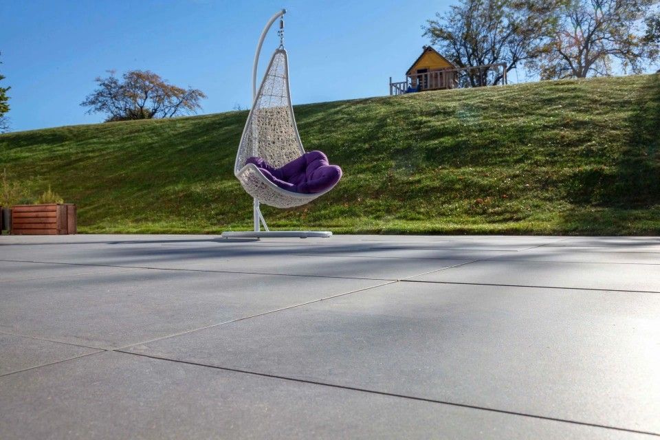 Une chaise suspendue avec un coussin violet se trouve sur un patio