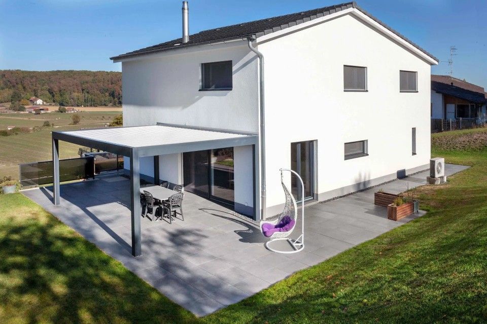 Une maison blanche avec une pergola et une chaise violette sur le patio.