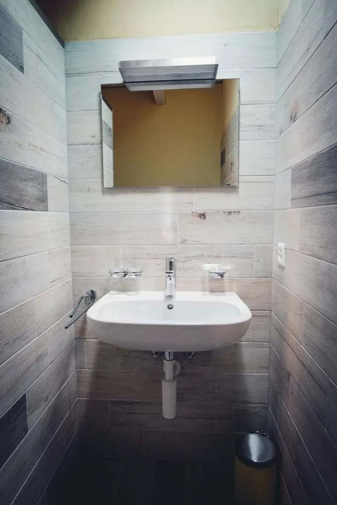 Une salle de bain avec lavabo , miroir et poubelle.