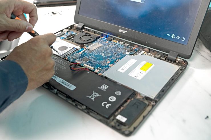 Une personne utilise un petit tournevis pour réparer les composants internes d'un ordinateur portable Acer ouvert, sur une surface blanche.