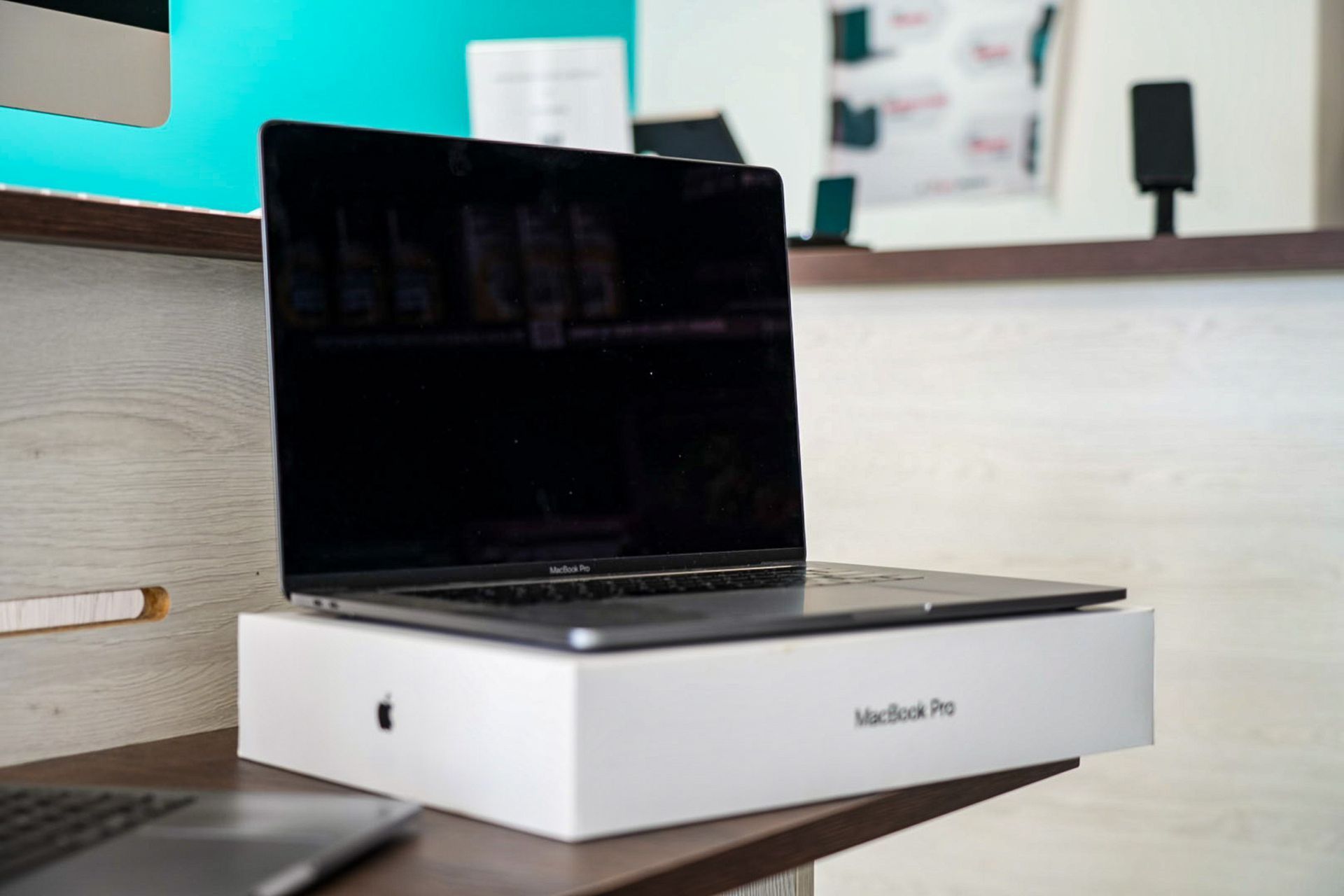 Un MacBook Pro gris est posé ouvert sur son emballage blanc, lui-même posé sur un bureau en bois.
