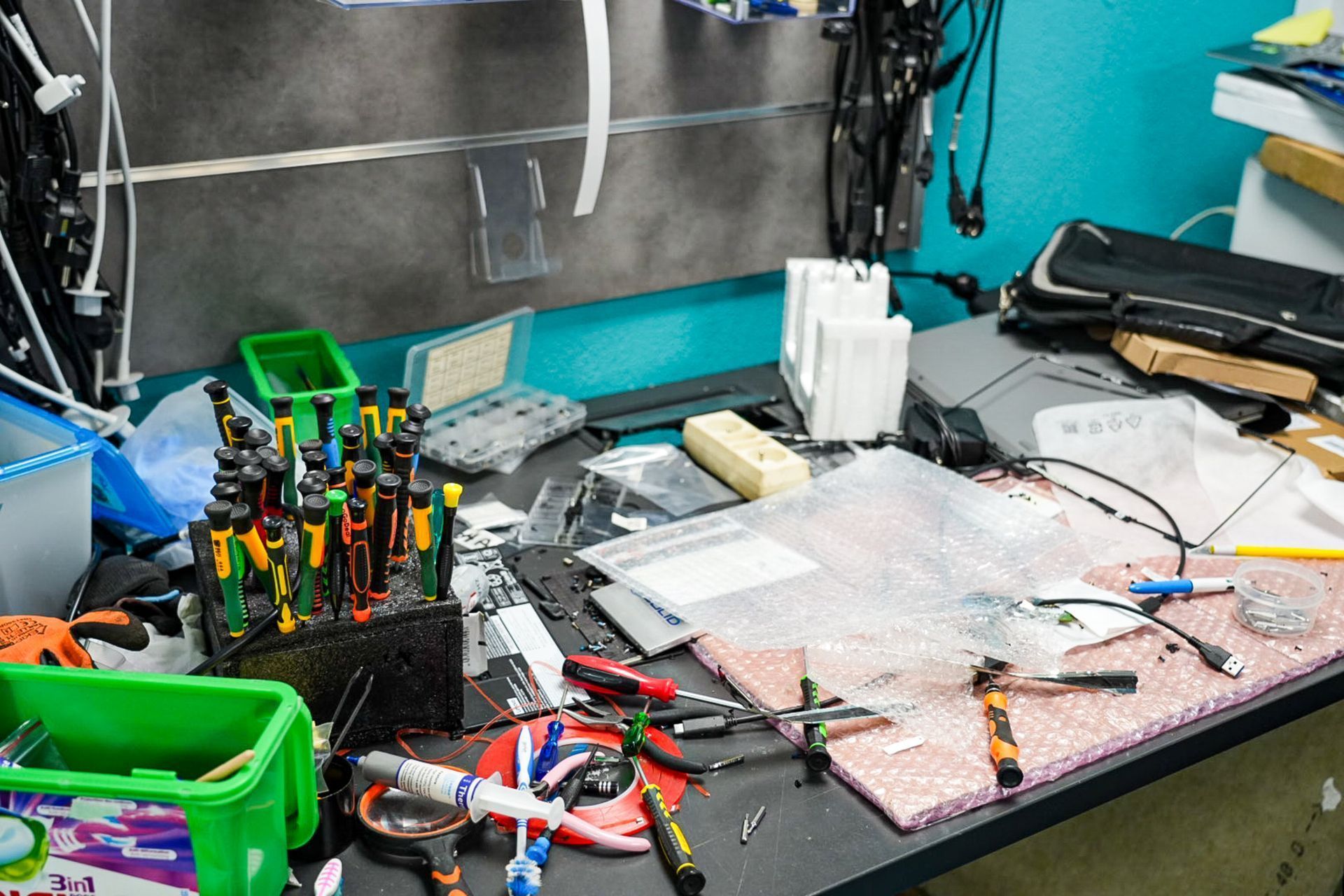 Un établi d'électronique encombré, avec de nombreux tournevis, outils et composants épars éparpillés sur toute sa surface.