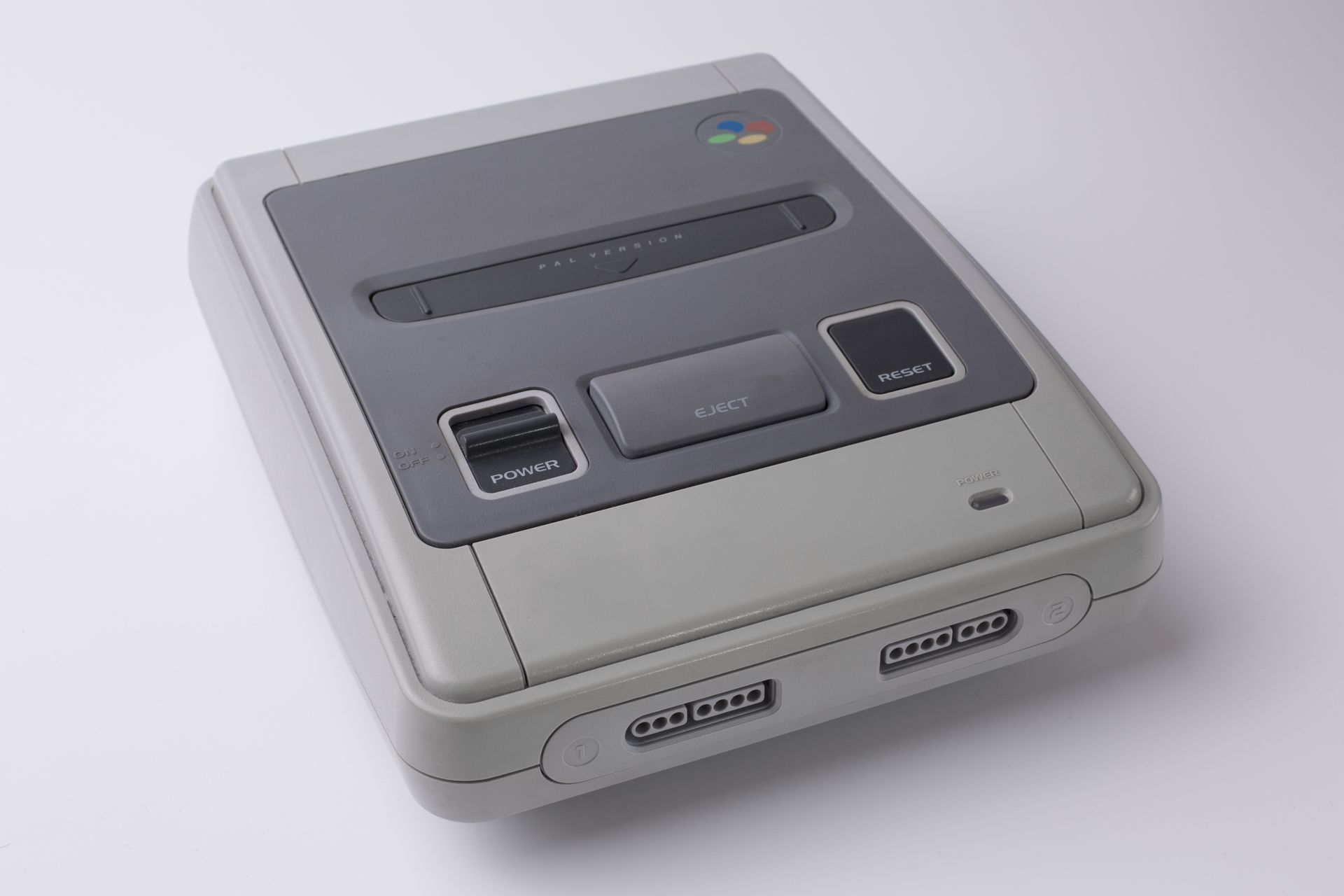 Une console de jeux Nintendo Super Famicom grise sur fond blanc, vue en plongée.