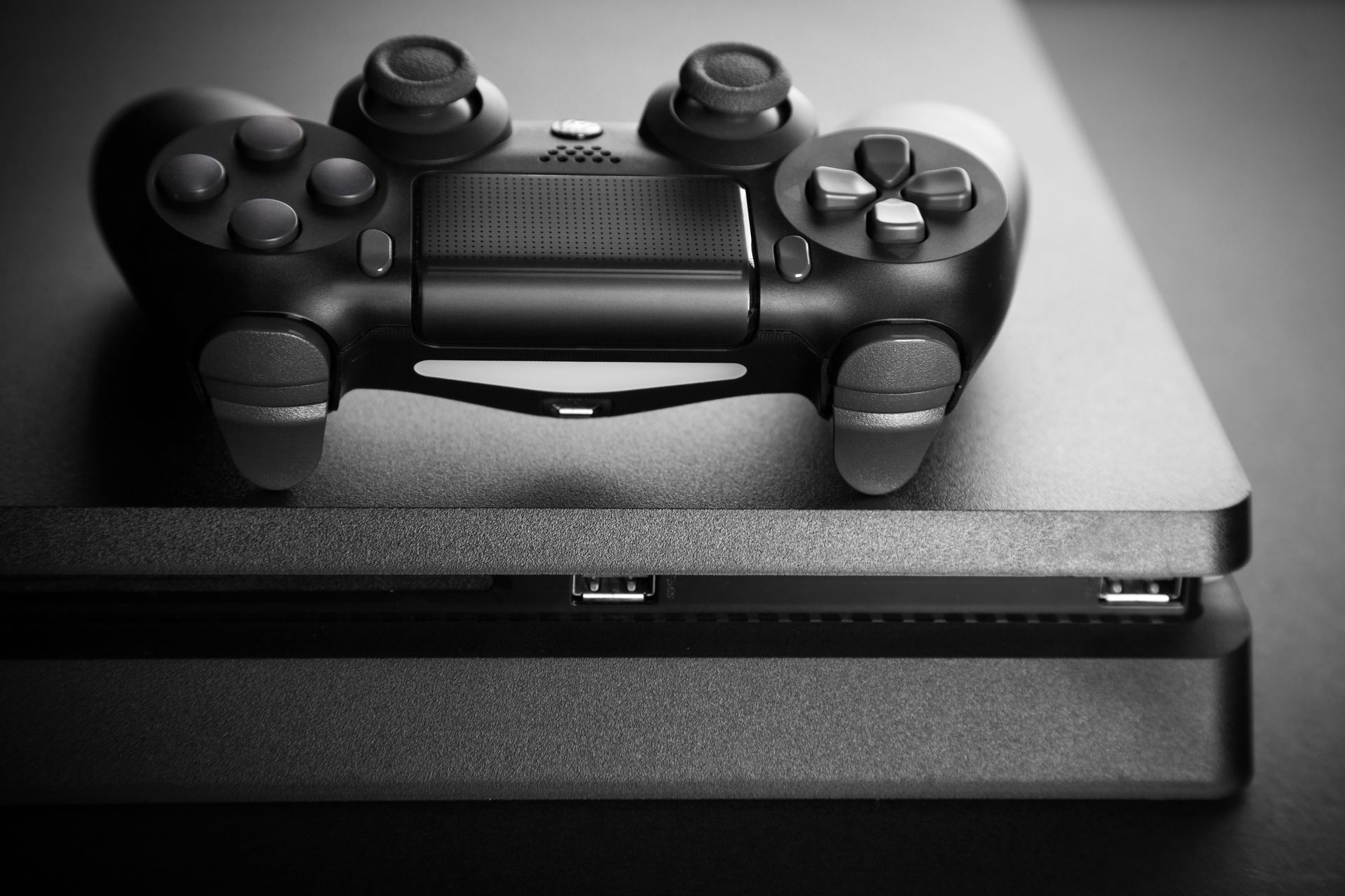 Une console PlayStation 4 noire avec une manette sans fil DualShock 4 assortie posée dessus, sur un fond sombre.