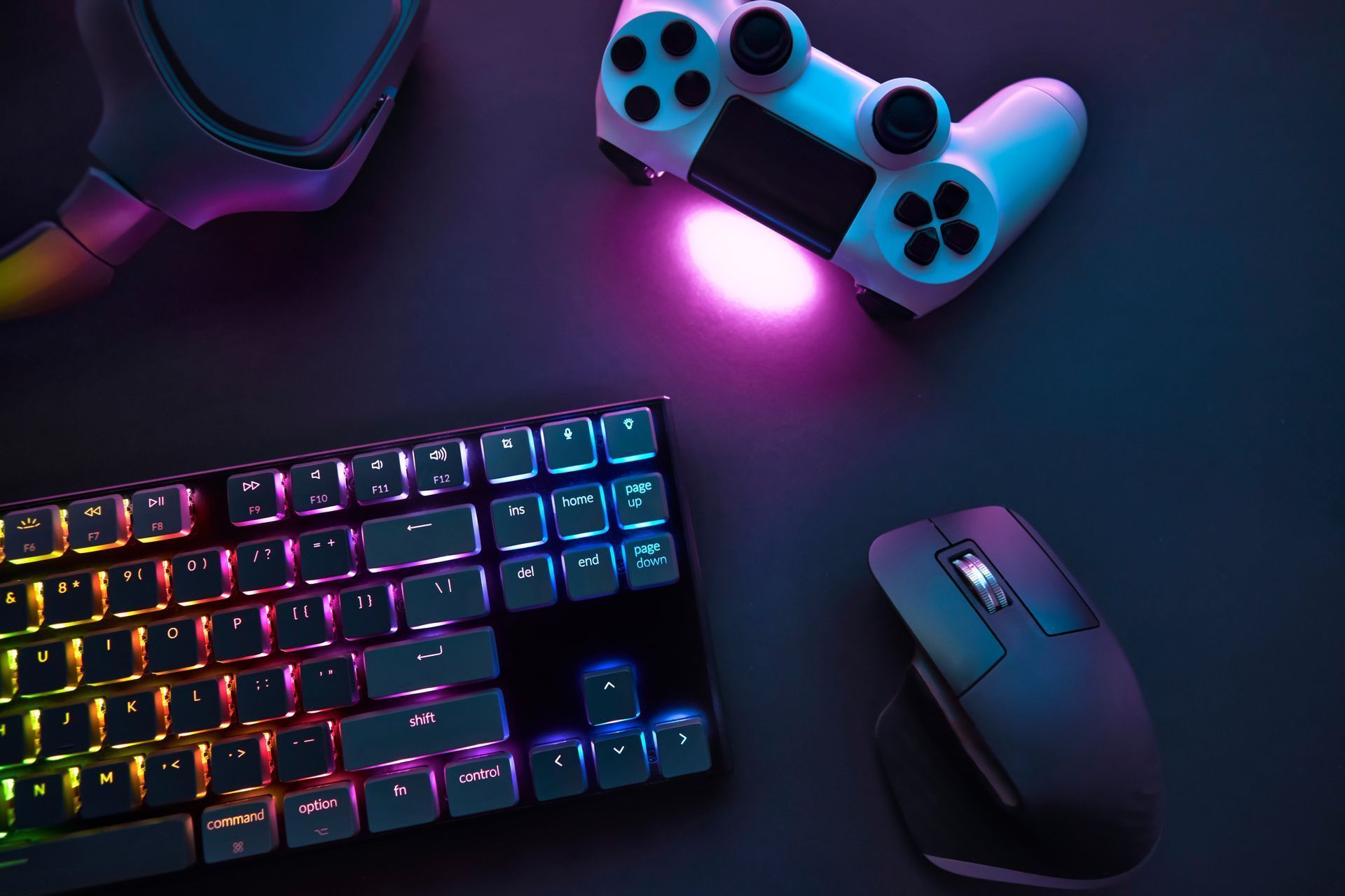 Configuration de jeu comprenant un clavier RGB multicolore, une souris noire et une manette de jeu blanche sur une surface sombre.