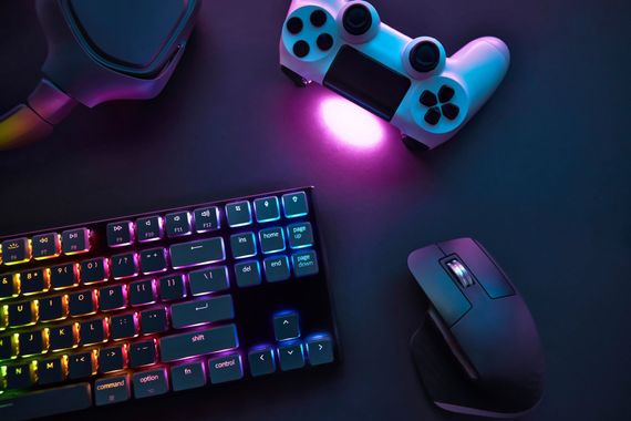 Configuration de jeu comprenant un clavier RGB multicolore, une souris noire et une manette de jeu blanche sur une surface sombre.