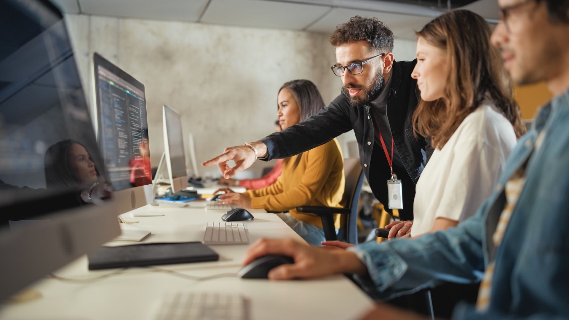 Un mentor désigne un écran d'ordinateur tout en guidant une équipe de collègues à leurs bureaux dans un espace de travail collaboratif.