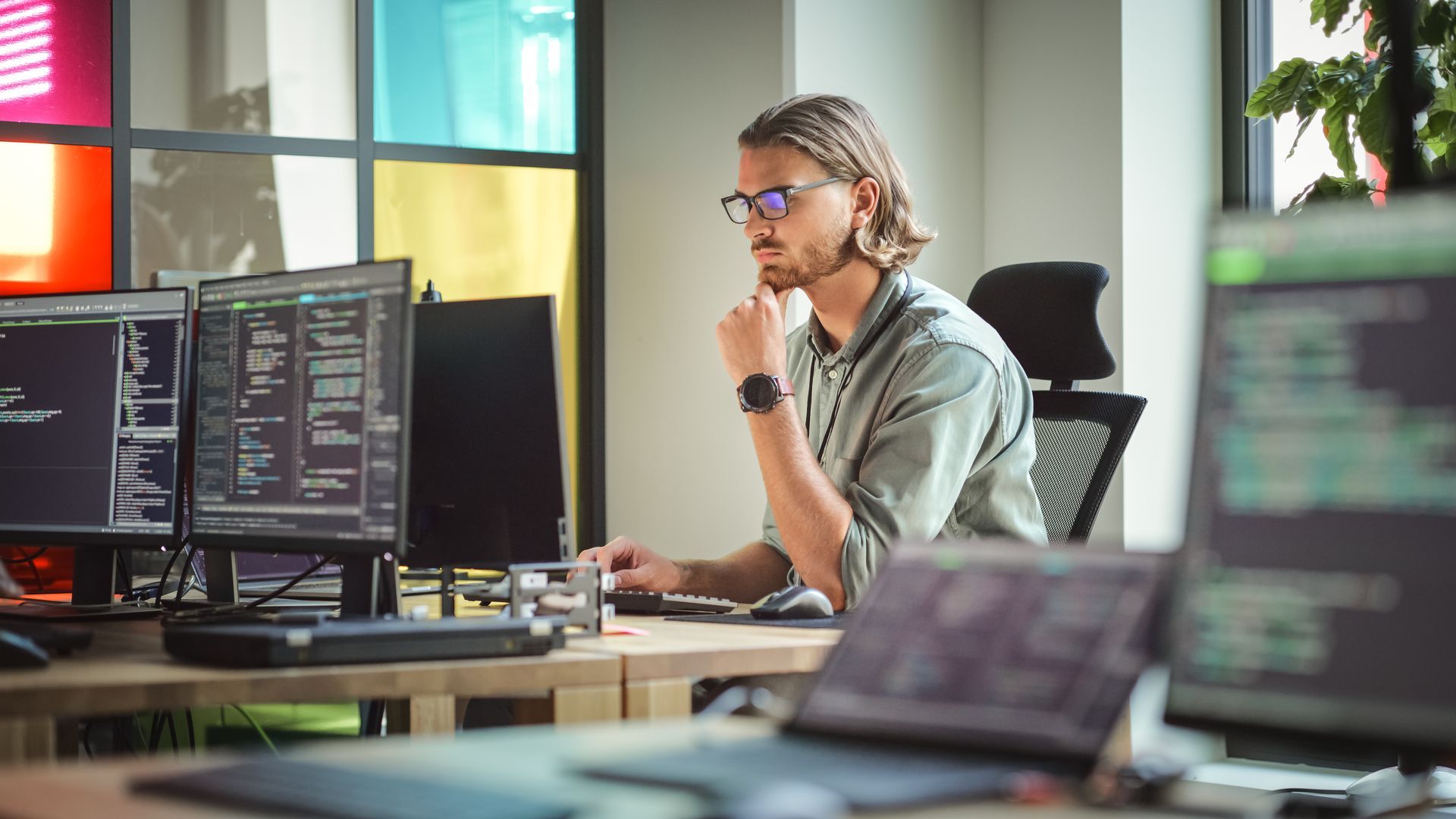 Une personne assise à un bureau, les yeux rivés sur un écran d'ordinateur affichant du code, dans un espace de travail équipé de plusieurs écrans.