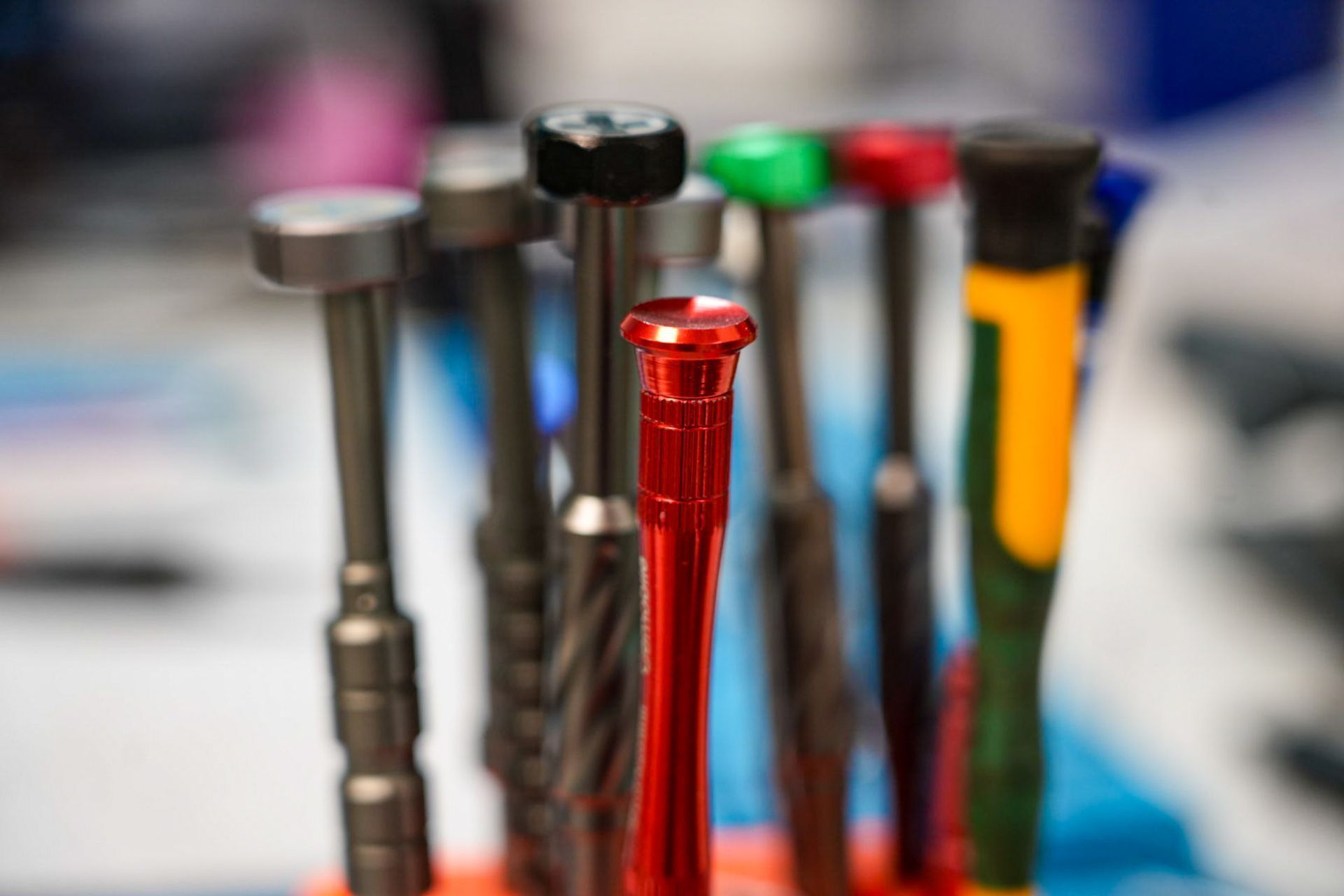 Gros plan sur plusieurs tournevis de précision colorés, disposés verticalement sur un support, avec un focus sur un tournevis rouge vif.