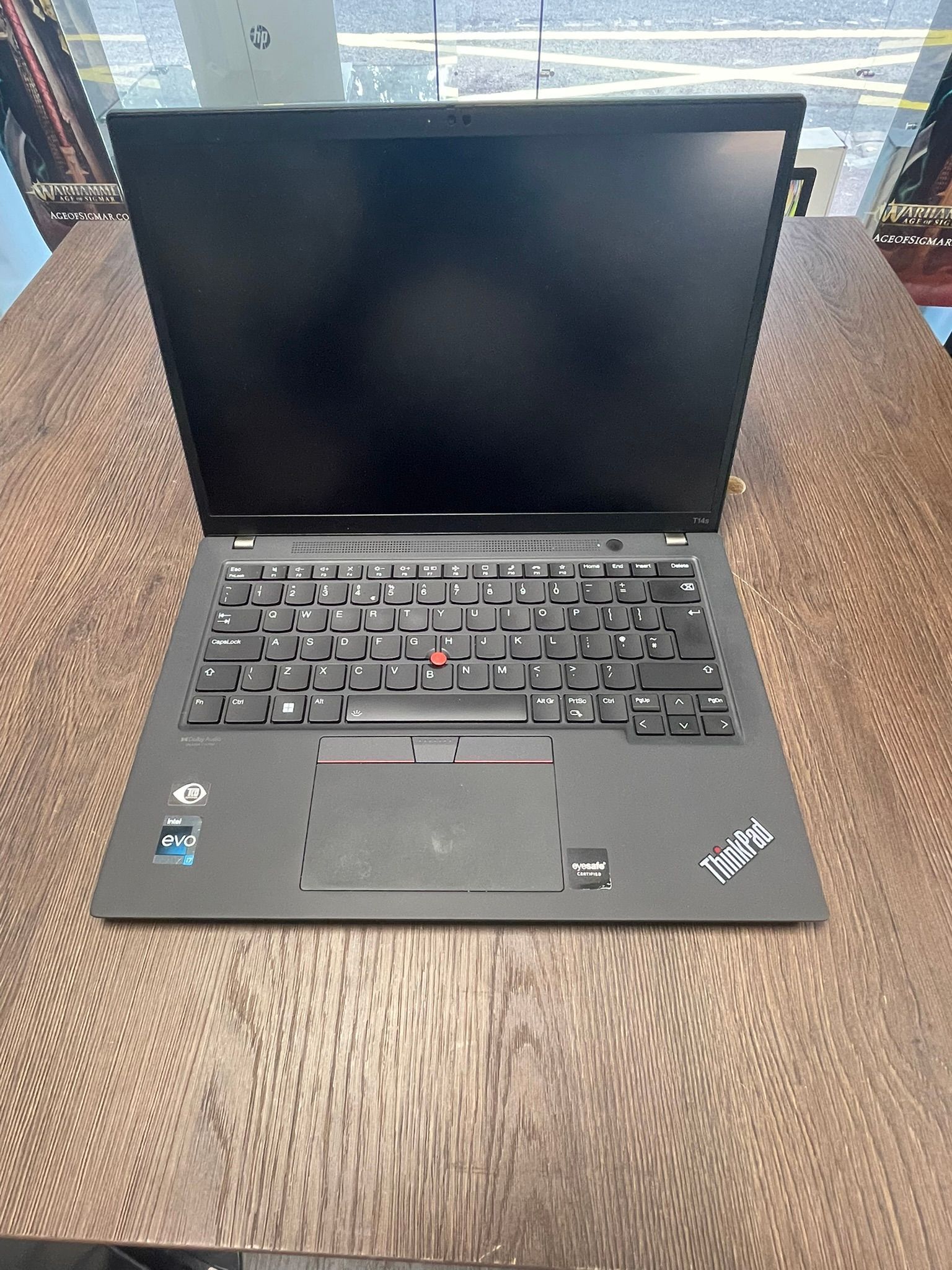 Ordinateur portable Lenovo ThinkPad noir ouvert sur une table en bois, écran éteint.