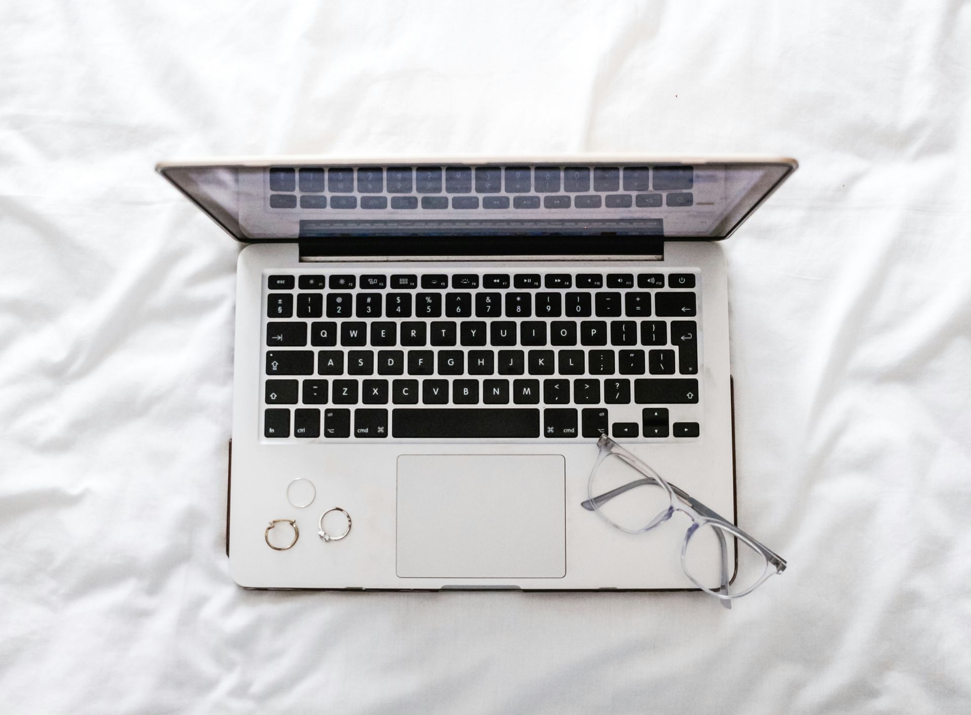 Vue de dessus d'un ordinateur portable argenté posé sur un tissu blanc, avec des lunettes et une tasse à proximité.
